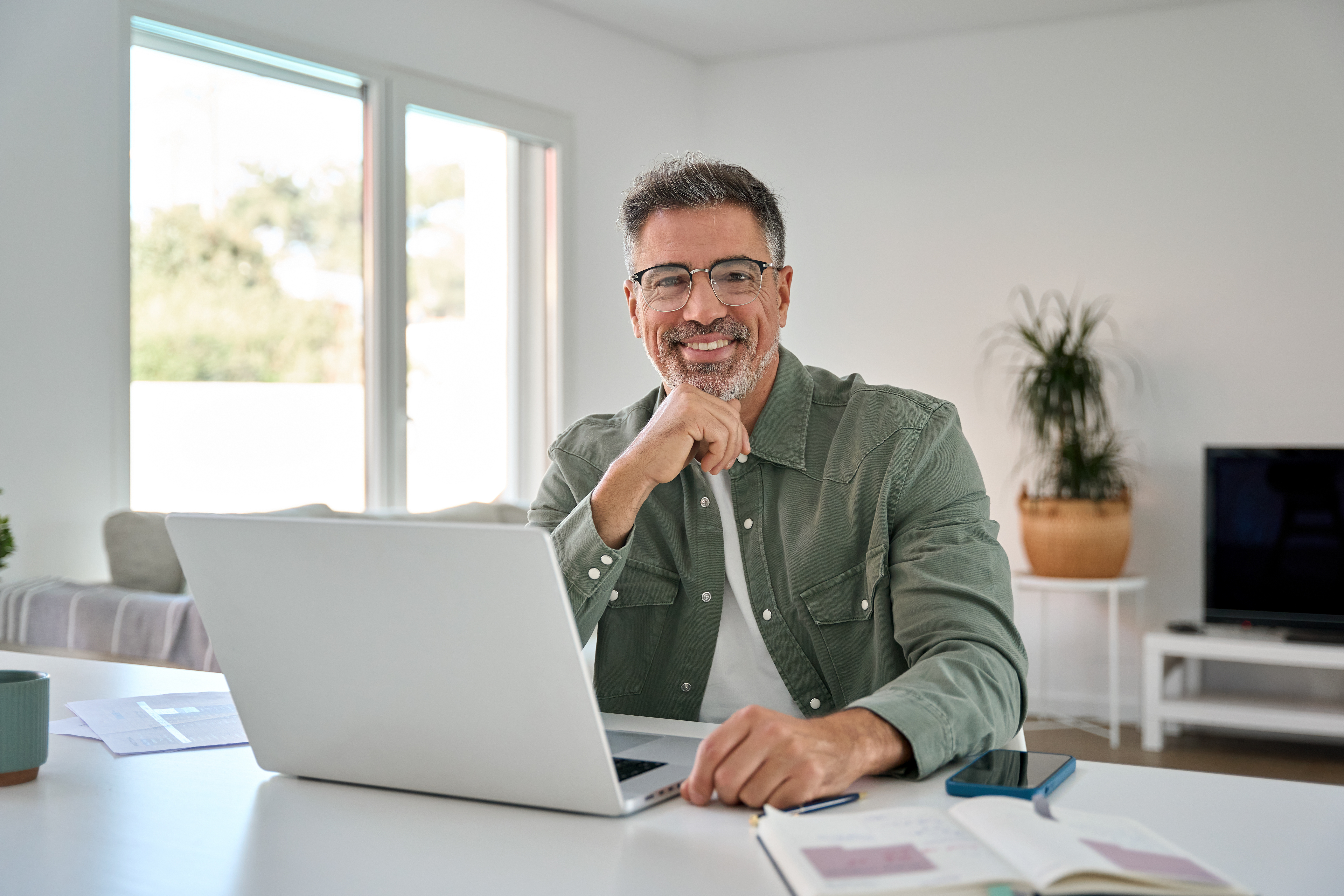 Mitarbeiter sitzt am Laptop und lächelt in die Kamera